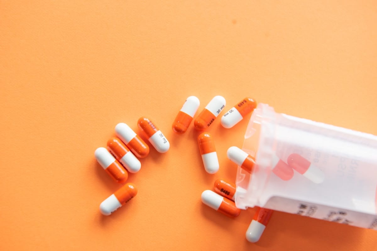 Orange pill capsules spilling from a bottle on an orange background