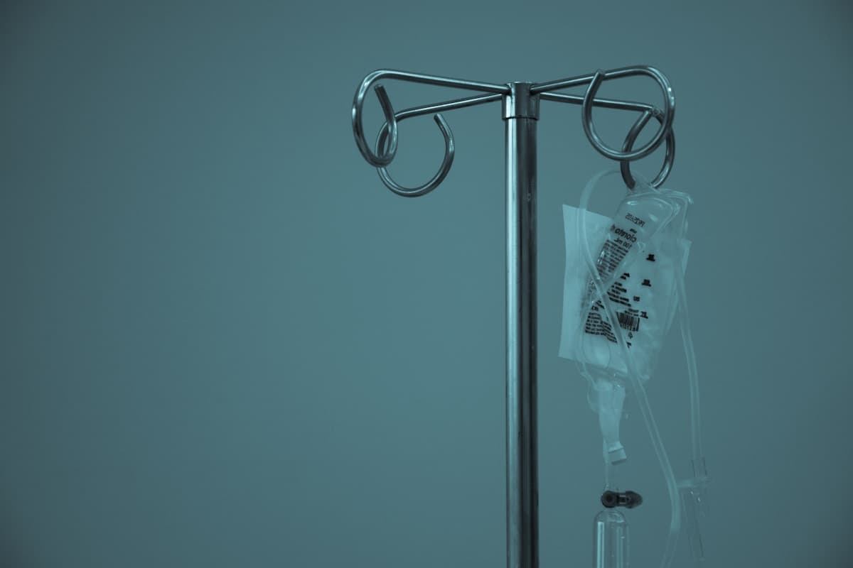 An IV drip stand against a teal wall