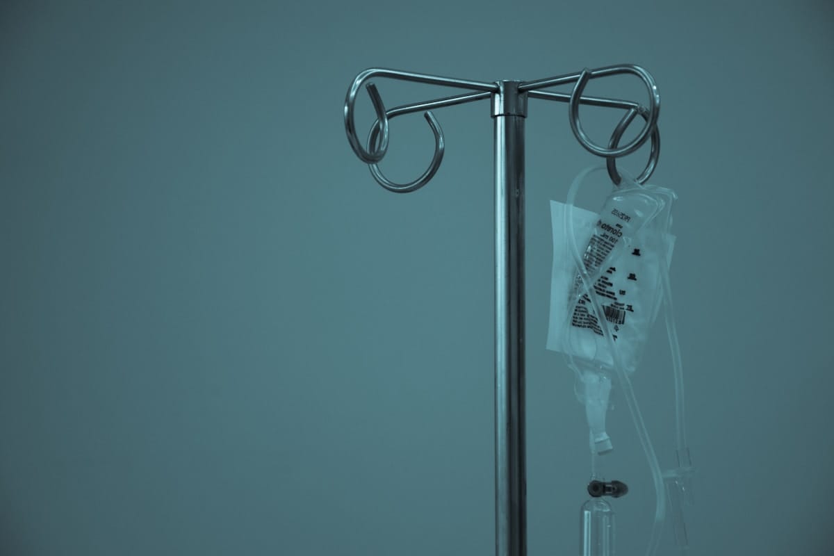 An IV drip stand against a teal wall